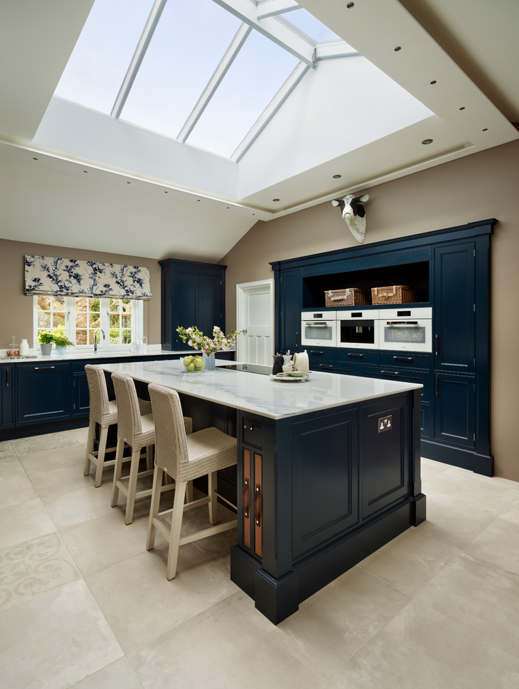 Design ideas for a mid-sized traditional kitchen in Essex with blue cabinets, marble benchtops, white appliances, with island, shaker cabinets and beige floor.