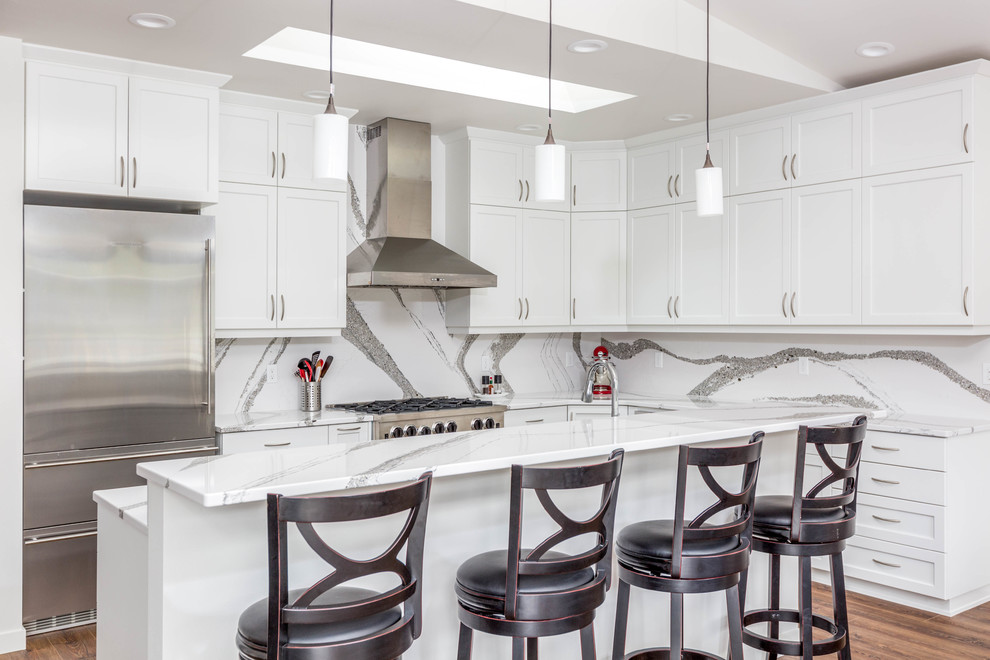 This is an example of a transitional l-shaped kitchen in Seattle with shaker cabinets, white cabinets, multi-coloured splashback, stone slab splashback, stainless steel appliances, medium hardwood floors, with island and multi-coloured benchtop.
