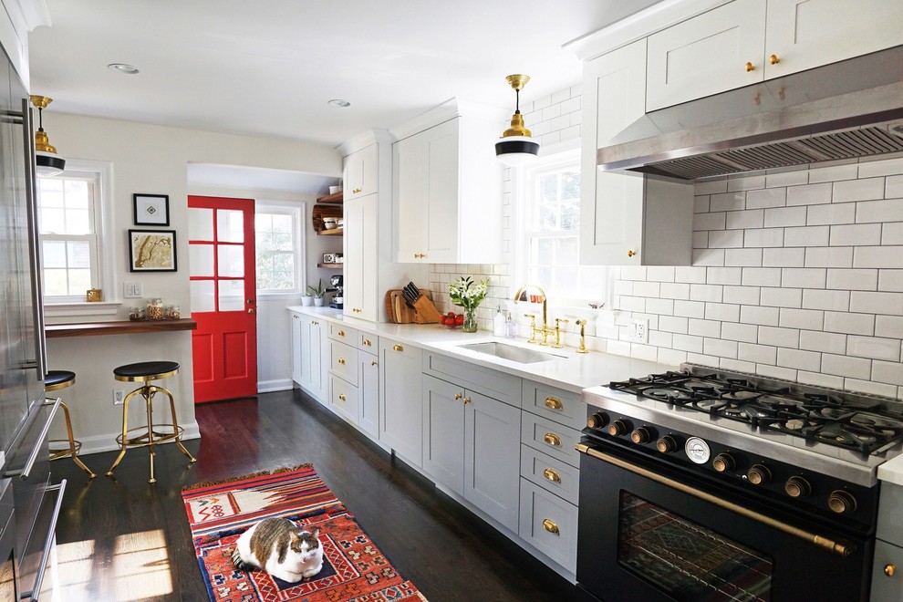 Photo of a mid-sized traditional kitchen in New York with grey cabinets, white splashback, subway tile splashback, black appliances, dark hardwood floors, no island, brown floor, a single-bowl sink and shaker cabinets.