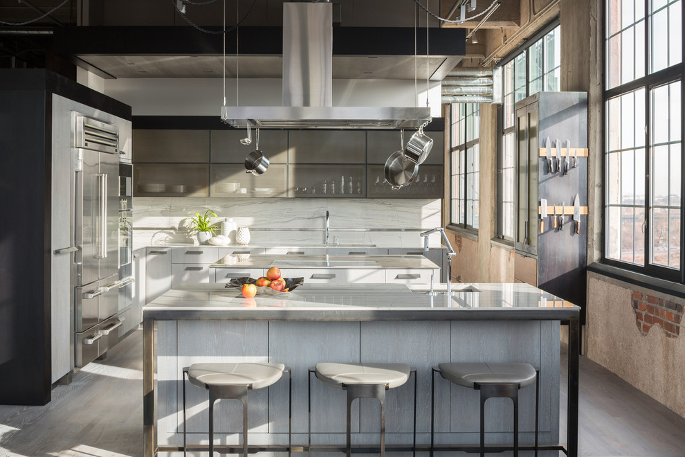 Industrial kitchen in Denver with an undermount sink, white splashback, stainless steel appliances, light hardwood floors and multiple islands.