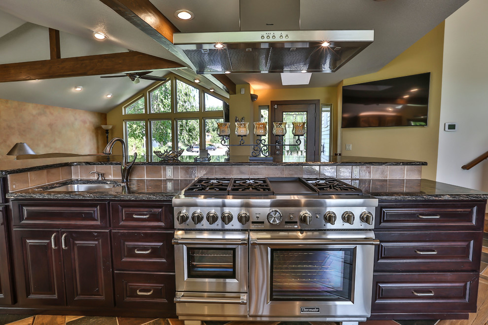 This is an example of a large country l-shaped eat-in kitchen in Seattle with an undermount sink, beaded inset cabinets, light wood cabinets, solid surface benchtops, brown splashback, glass tile splashback, stainless steel appliances, medium hardwood floors, with island and brown floor.
