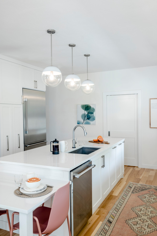 Large transitional l-shaped light wood floor and brown floor eat-in kitchen photo in Austin with a single-bowl sink, shaker cabinets, white cabinets, quartz countertops, white backsplash, ceramic backsplash, stainless steel appliances, an island and white countertops