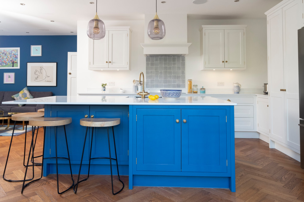 Example of a mid-sized classic l-shaped light wood floor open concept kitchen design in Cardiff with a farmhouse sink, shaker cabinets, blue cabinets, multicolored backsplash, porcelain backsplash, stainless steel appliances, an island and white countertops