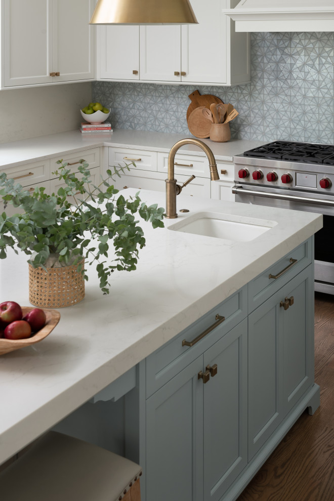 Design ideas for a large beach style u-shaped kitchen pantry in Chicago with a farmhouse sink, shaker cabinets, white cabinets, quartz benchtops, blue splashback, glass tile splashback, panelled appliances, medium hardwood floors, with island, brown floor and white benchtop.