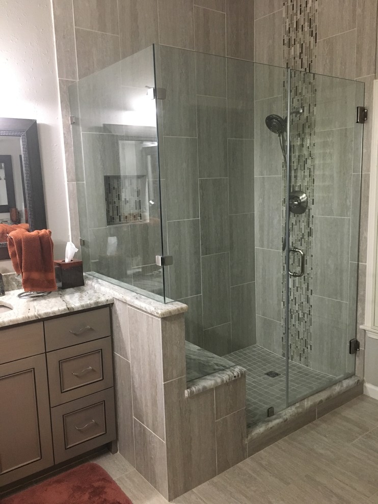 This is an example of a mid-sized contemporary master bathroom in Austin with recessed-panel cabinets, grey cabinets, a corner shower, gray tile, porcelain tile, grey walls, porcelain floors, an undermount sink, marble benchtops, grey floor and a hinged shower door.