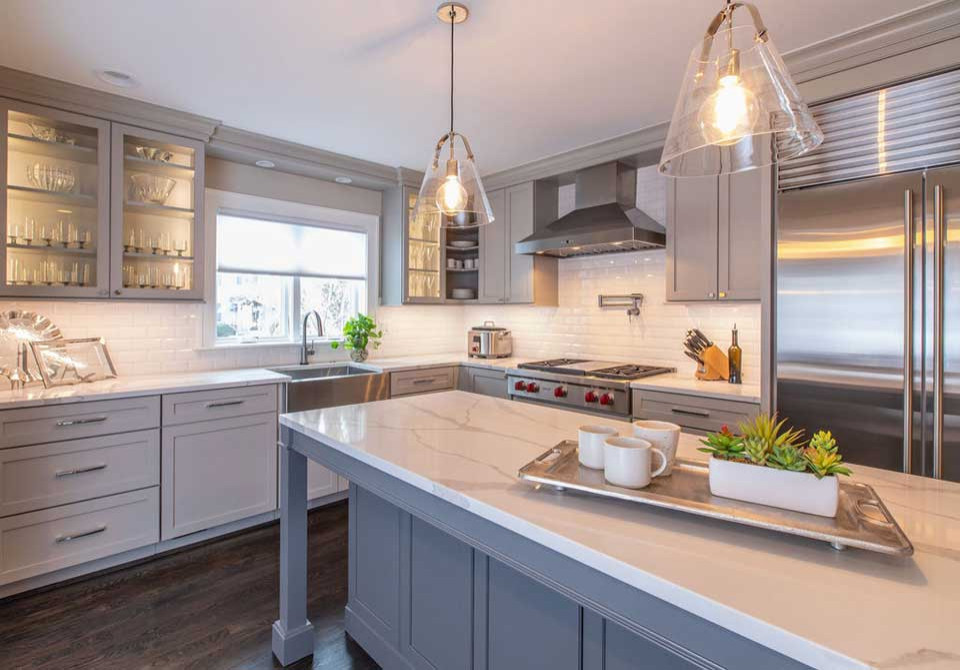 Photo of a large transitional l-shaped separate kitchen in Detroit with a farmhouse sink, shaker cabinets, grey cabinets, quartz benchtops, white splashback, subway tile splashback, stainless steel appliances, dark hardwood floors, with island, brown floor and white benchtop.