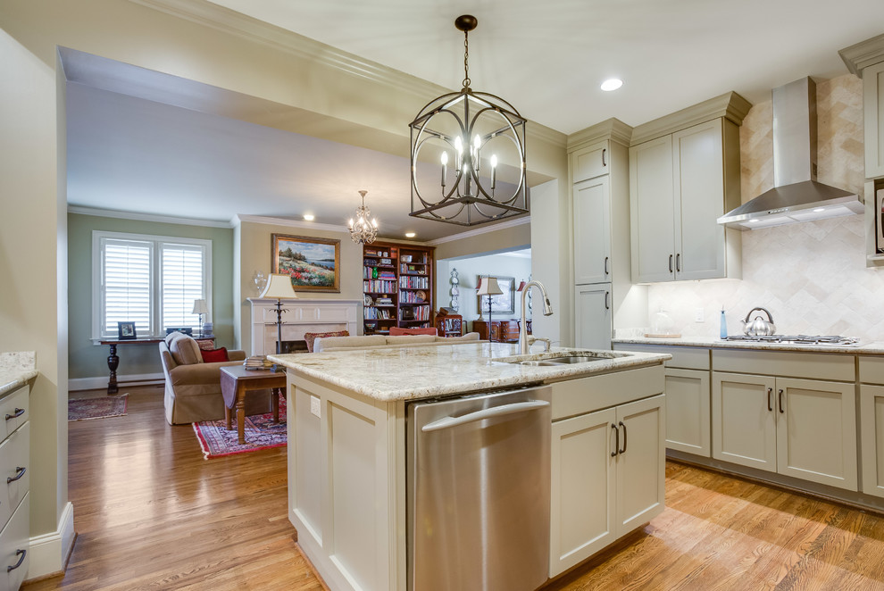Example of a transitional u-shaped medium tone wood floor and brown floor enclosed kitchen design in Birmingham with a double-bowl sink, shaker cabinets, beige cabinets, granite countertops, beige backsplash, travertine backsplash, stainless steel appliances and an island