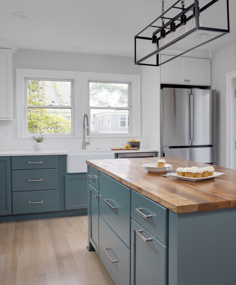 Inspiration for a medium sized classic l-shaped kitchen in DC Metro with a belfast sink, shaker cabinets, green cabinets, engineered stone countertops, white splashback, ceramic splashback, stainless steel appliances, light hardwood flooring, an island, white worktops and exposed beams.