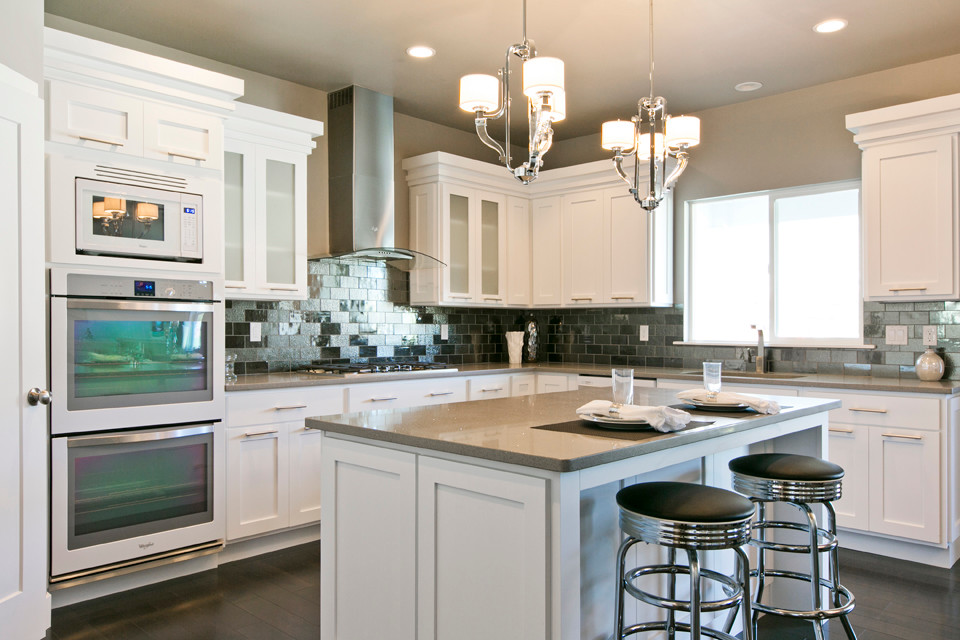 This is an example of a large transitional l-shaped eat-in kitchen in Salt Lake City with a double-bowl sink, raised-panel cabinets, white cabinets, quartz benchtops, metallic splashback, glass tile splashback, white appliances, dark hardwood floors and with island.