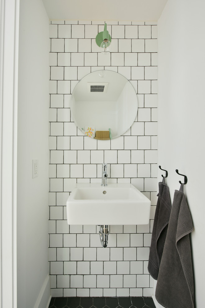 Small industrial powder room in Ottawa with white walls, a wall-mount sink, white tile, ceramic tile and black floor.