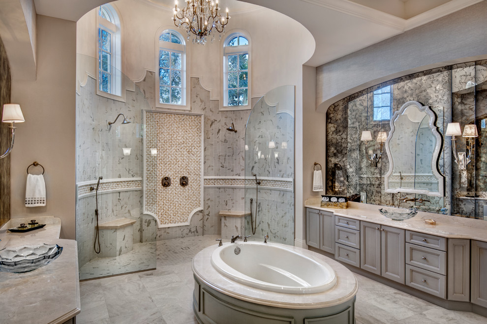 Large mediterranean master bathroom in Miami with recessed-panel cabinets, grey cabinets, a drop-in tub, an open shower, marble, beige walls, marble floors, a vessel sink, marble benchtops, beige floor and an open shower.