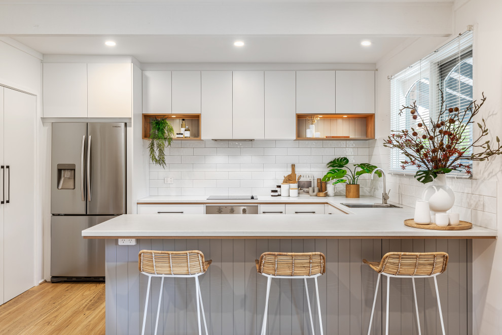 This is an example of a mid-sized contemporary u-shaped eat-in kitchen in Adelaide with a single-bowl sink, white cabinets, laminate benchtops, white splashback, subway tile splashback, stainless steel appliances, medium hardwood floors, a peninsula, brown floor and white benchtop.