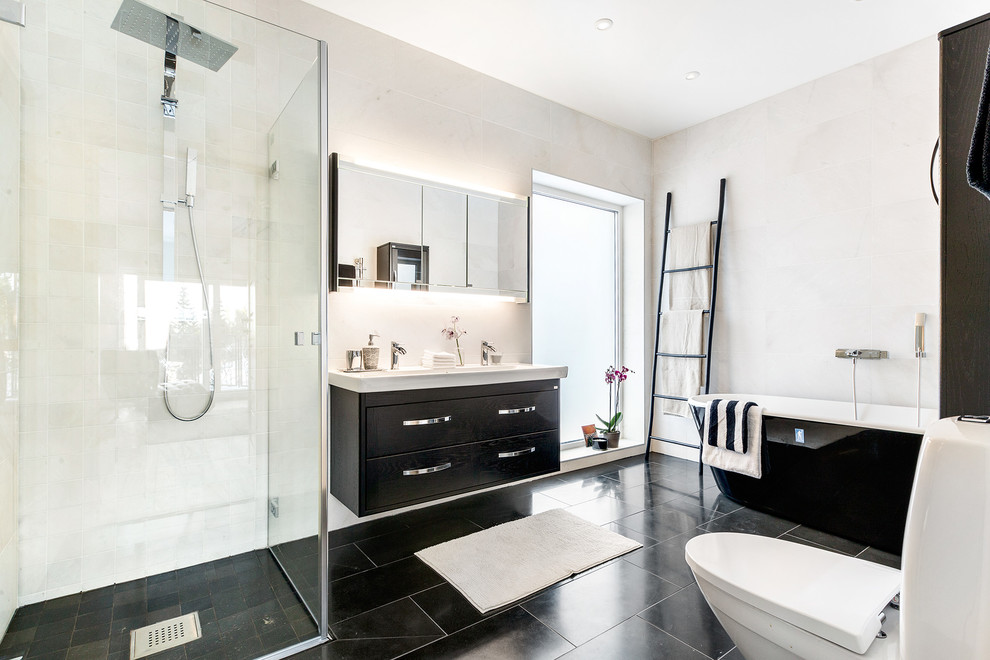 Design ideas for a large contemporary master bathroom in Stockholm with flat-panel cabinets, black cabinets, a freestanding tub, a corner shower, a two-piece toilet, beige walls, a console sink, ceramic floors and white tile.