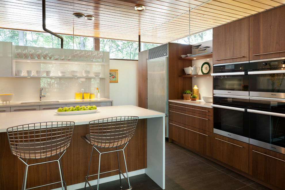 Mid-sized midcentury l-shaped kitchen pantry in DC Metro with an undermount sink, flat-panel cabinets, white cabinets, laminate benchtops, white splashback, with island and brown floor.