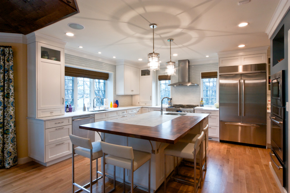 Eat-in kitchen - transitional medium tone wood floor eat-in kitchen idea in Newark with an undermount sink, recessed-panel cabinets, white cabinets, glass tile backsplash, stainless steel appliances, wood countertops, white backsplash and an island