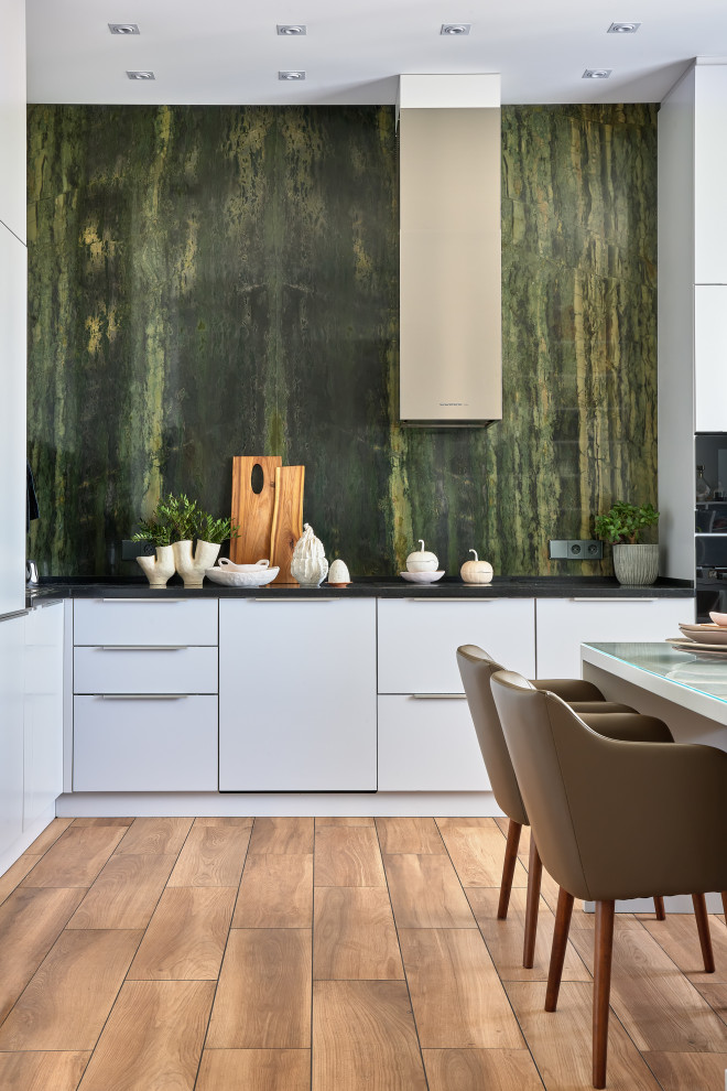 This is an example of a contemporary l-shaped eat-in kitchen in Moscow with flat-panel cabinets, white cabinets, black splashback, black appliances, no island, brown floor and green benchtop.