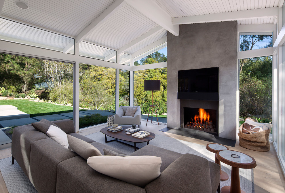 This is an example of a mid-sized contemporary open concept living room in Santa Barbara with white walls, light hardwood floors, a standard fireplace, a concrete fireplace surround and a wall-mounted tv.