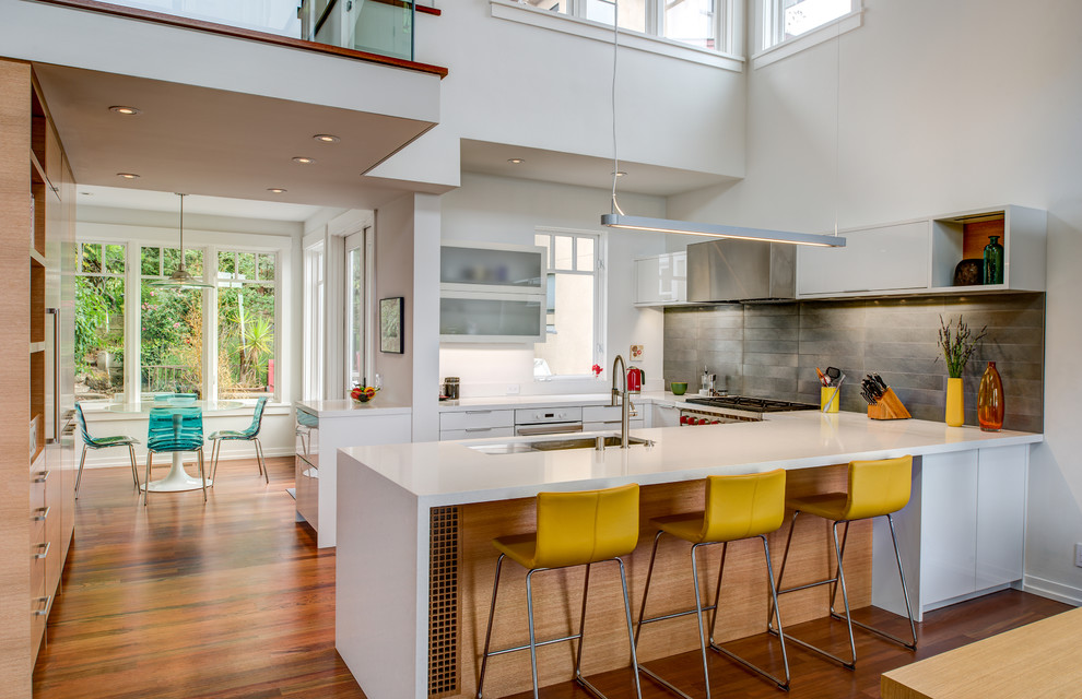 Expansive contemporary u-shaped eat-in kitchen in San Francisco with a double-bowl sink, flat-panel cabinets, white cabinets, grey splashback, stone tile splashback, medium hardwood floors, a peninsula and stainless steel appliances.