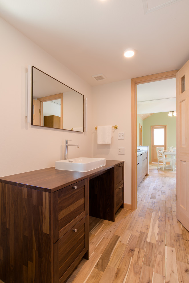 Photo of a mid-sized tropical powder room in Other with shaker cabinets, brown cabinets, white walls, medium hardwood floors, a vessel sink, wood benchtops, brown floor and brown benchtops.