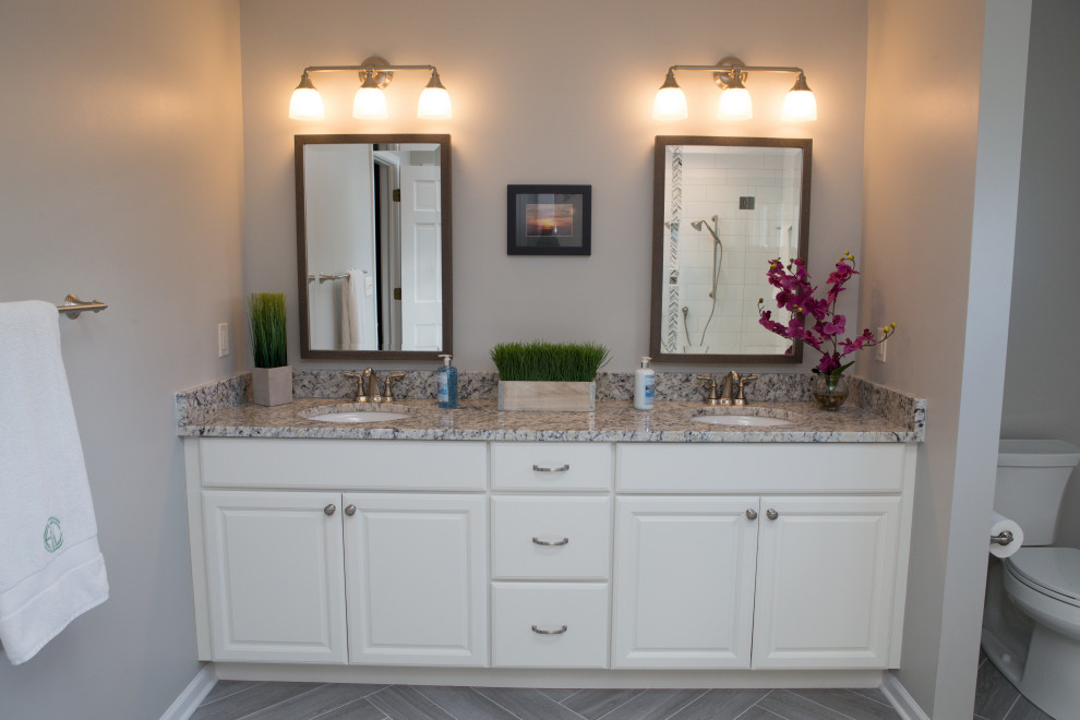 Large transitional master bathroom in Chicago with raised-panel cabinets, white cabinets, an alcove shower, a two-piece toilet, white tile, ceramic tile, grey walls, porcelain floors, an undermount sink, granite benchtops, grey floor, a hinged shower door, grey benchtops, a shower seat, a double vanity and a built-in vanity.