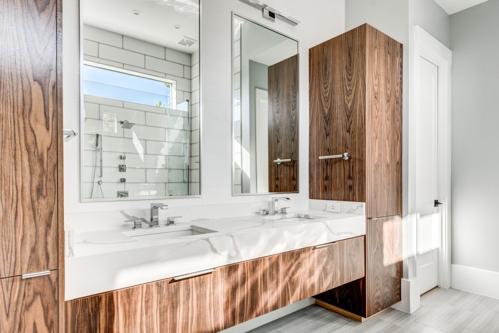 This is an example of a transitional master bathroom in Dallas with flat-panel cabinets, medium wood cabinets, a double shower, a one-piece toilet, white tile, porcelain tile, white walls, porcelain floors, an undermount sink, engineered quartz benchtops, grey floor, an open shower and white benchtops.