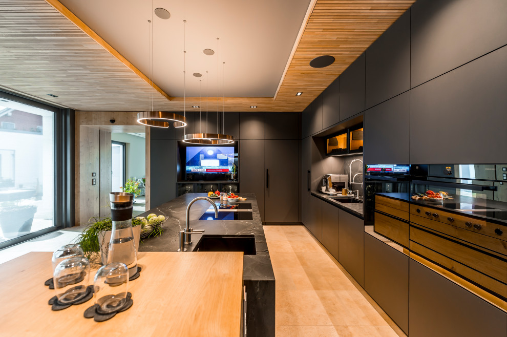 Example of a large trendy l-shaped beige floor and wood ceiling open concept kitchen design in Leipzig with an undermount sink, gray cabinets, gray backsplash, stone slab backsplash, black appliances, an island and gray countertops