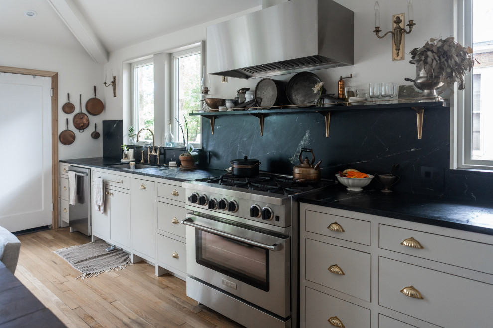 Inspiration for a transitional galley medium tone wood floor, brown floor and vaulted ceiling kitchen remodel in Austin with an undermount sink, flat-panel cabinets, gray cabinets, black backsplash, stone slab backsplash, stainless steel appliances and black countertops