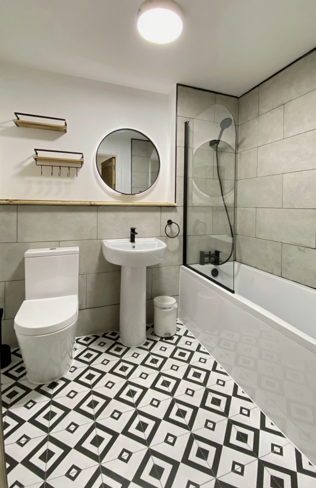 This is an example of a mid-sized contemporary kids bathroom in London with a drop-in tub, a one-piece toilet, gray tile, ceramic tile, white walls, ceramic floors, a pedestal sink, wood benchtops, a single vanity and a built-in vanity.