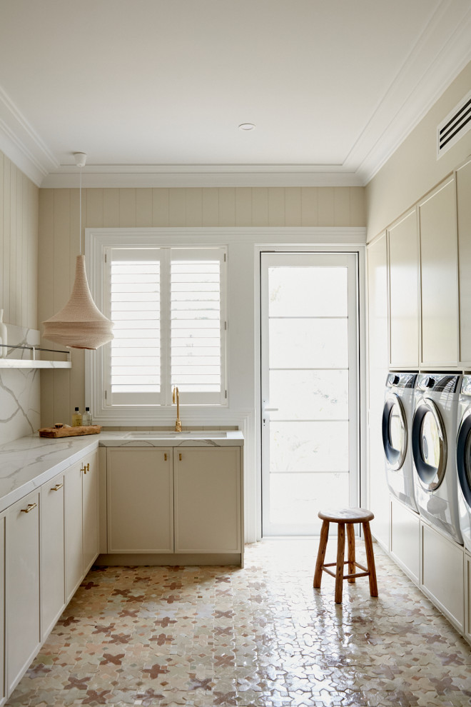 Foto på en stor rustik vita tvättstuga, med beige skåp, marmorbänkskiva, vitt stänkskydd, stänkskydd i marmor, beige väggar, klinkergolv i keramik, en tvättmaskin och torktumlare bredvid varandra och flerfärgat golv