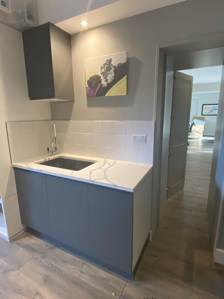 Design ideas for a large contemporary galley utility room in London with a drop-in sink, flat-panel cabinets, grey cabinets, quartzite benchtops, white splashback, porcelain splashback, beige walls, laminate floors, a side-by-side washer and dryer, grey floor and multi-coloured benchtop.