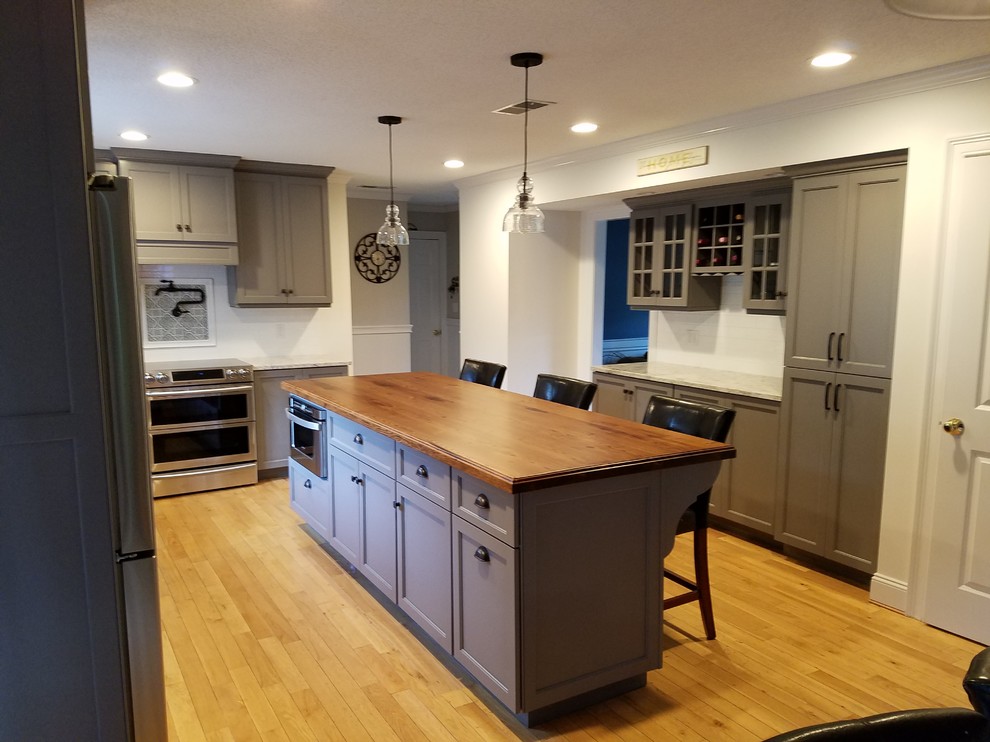 Mid-sized transitional galley light wood floor and brown floor eat-in kitchen photo with a farmhouse sink, recessed-panel cabinets, gray cabinets, wood countertops, white backsplash, subway tile backsplash, stainless steel appliances and an island
