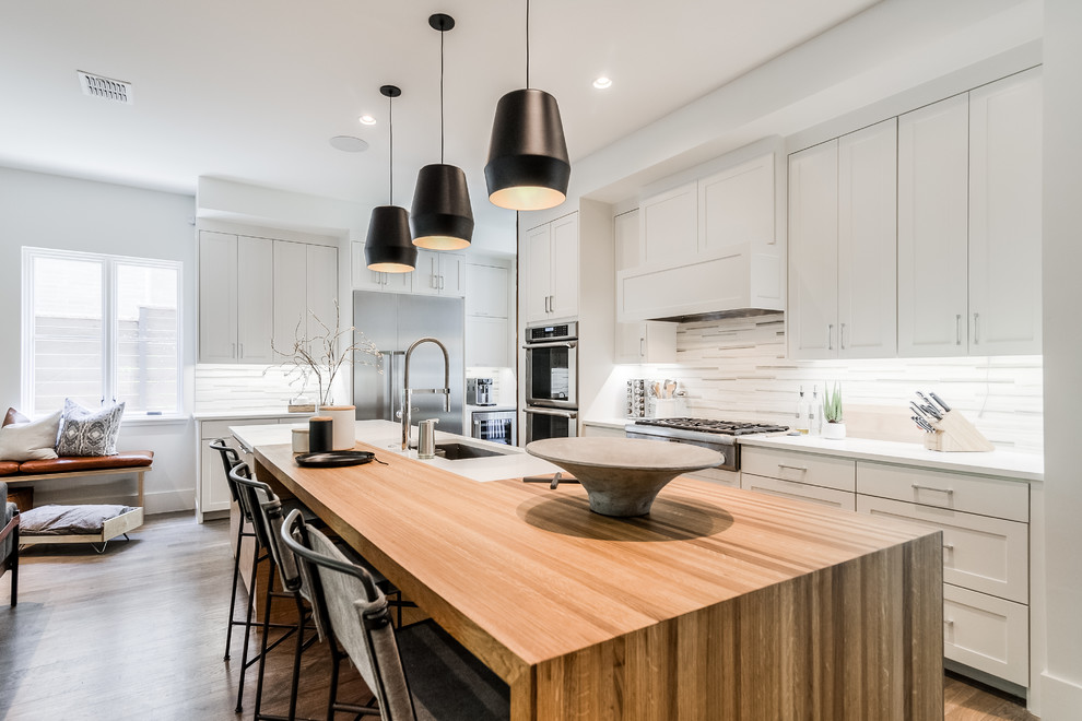 Large contemporary l-shaped open plan kitchen in Dallas with an undermount sink, shaker cabinets, white cabinets, multi-coloured splashback, stainless steel appliances, with island, white benchtop and medium hardwood floors.