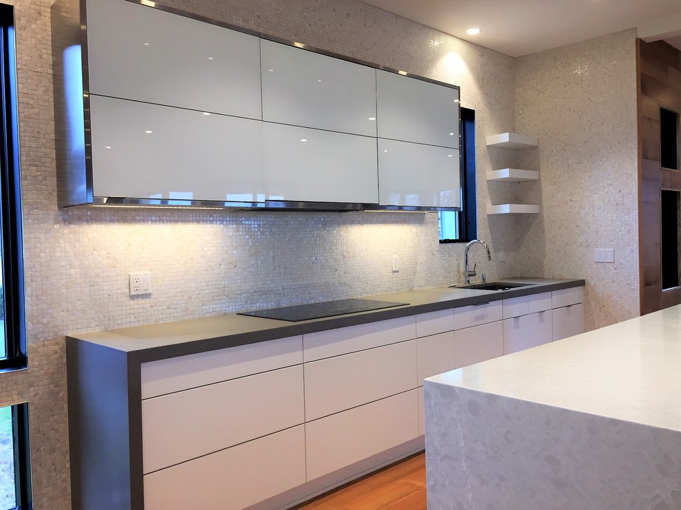 This is an example of a contemporary eat-in kitchen in New York with flat-panel cabinets, white cabinets, quartz benchtops, stainless steel appliances, medium hardwood floors, with island and grey benchtop.