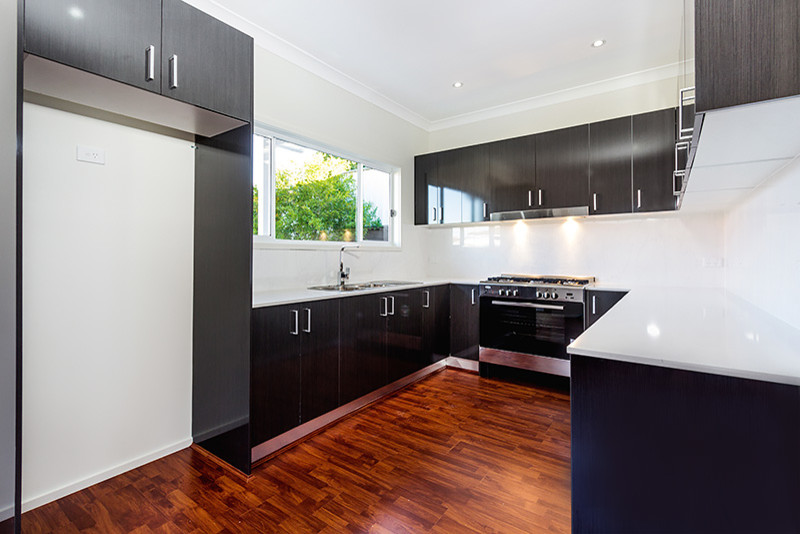 Inspiration for a mid-sized contemporary u-shaped kitchen pantry in Sydney with a drop-in sink, flat-panel cabinets, dark wood cabinets, white splashback, ceramic splashback, stainless steel appliances, laminate floors and no island.