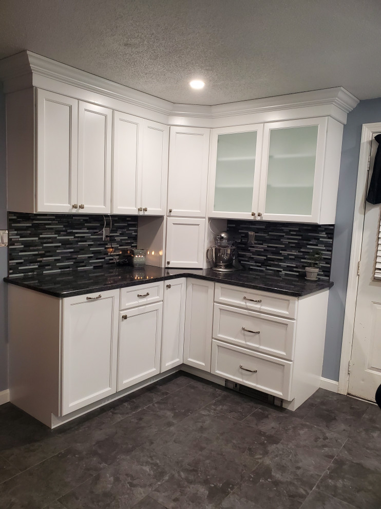 Photo of a mid-sized modern l-shaped eat-in kitchen in Boston with a single-bowl sink, flat-panel cabinets, white cabinets, granite benchtops, multi-coloured splashback, glass sheet splashback, stainless steel appliances, vinyl floors, no island, grey floor and grey benchtop.