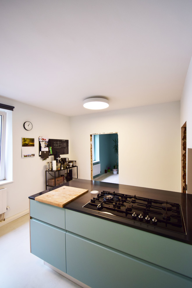 Photo of a mid-sized modern galley open plan kitchen in Cologne with an undermount sink, flat-panel cabinets, turquoise cabinets, black splashback, glass sheet splashback, black appliances, concrete floors, with island, grey floor and black benchtop.
