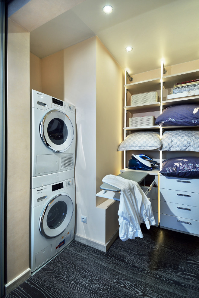 This is an example of a mid-sized contemporary single-wall laundry cupboard in Other with flat-panel cabinets, white cabinets, cork floors, a stacked washer and dryer, black floor and beige benchtop.