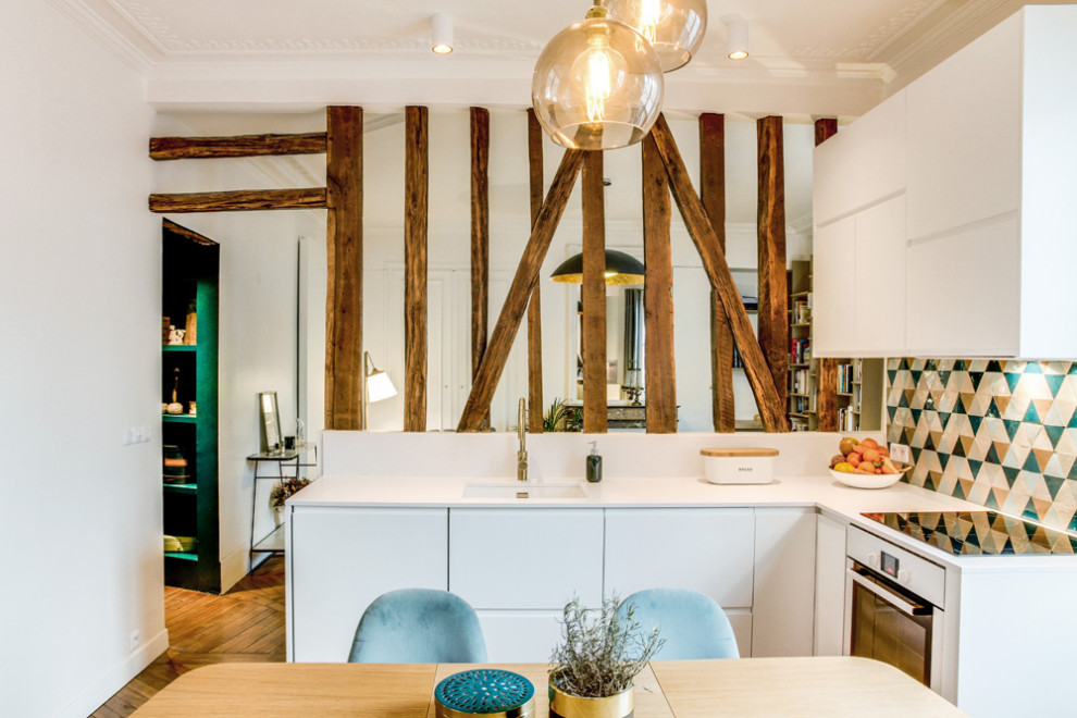 Mid-sized contemporary single-wall open plan kitchen in Paris with an undermount sink, flat-panel cabinets, white cabinets, multi-coloured splashback, terra-cotta splashback, panelled appliances, light hardwood floors, no island, brown floor and white benchtop.