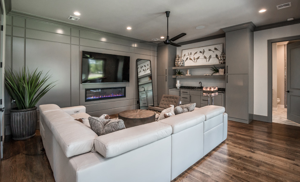 This is an example of an expansive transitional enclosed family room in Other with grey walls, medium hardwood floors, a ribbon fireplace, a wood fireplace surround, a wall-mounted tv and brown floor.