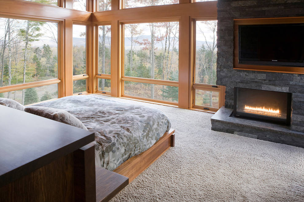 Example of a large mountain style master carpeted bedroom design with a corner fireplace, a stone fireplace and gray walls