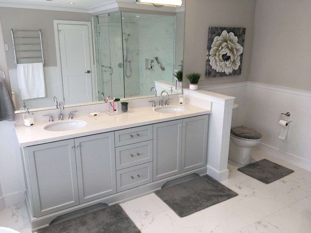 Photo of an expansive transitional master bathroom in Toronto with recessed-panel cabinets, grey cabinets, a freestanding tub, a corner shower, a two-piece toilet, white tile, porcelain tile, grey walls, porcelain floors, an undermount sink, engineered quartz benchtops, white floor, a hinged shower door and white benchtops.
