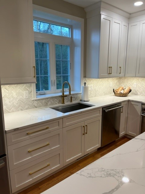 Large transitional l-shaped medium tone wood floor and brown floor eat-in kitchen photo in Boston with an undermount sink, shaker cabinets, white cabinets, quartz countertops, white backsplash, stainless steel appliances, an island and white countertops