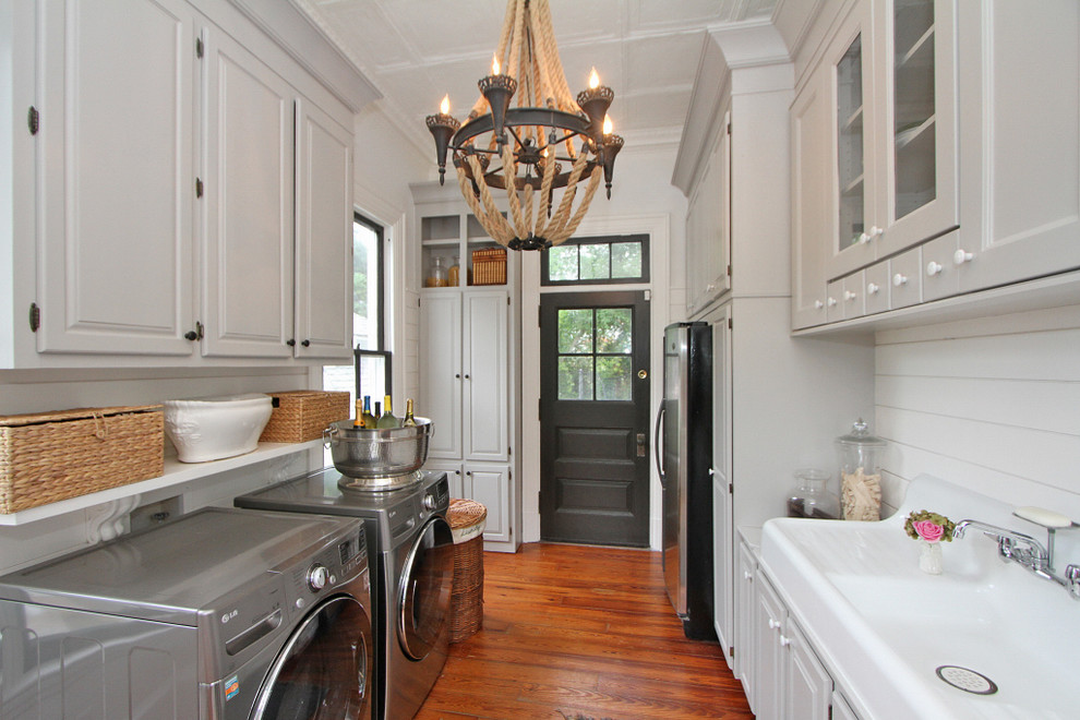 Photo of a mid-sized transitional galley utility room in Charleston with raised-panel cabinets, white cabinets, marble benchtops, white walls, medium hardwood floors, a side-by-side washer and dryer, brown floor and a drop-in sink.