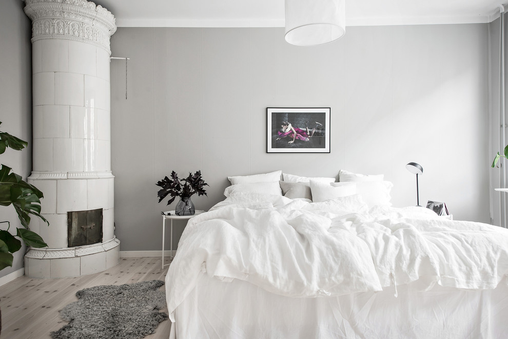 Photo of a mid-sized scandinavian master bedroom in Gothenburg with grey walls, light hardwood floors, a corner fireplace, a tile fireplace surround and grey floor.