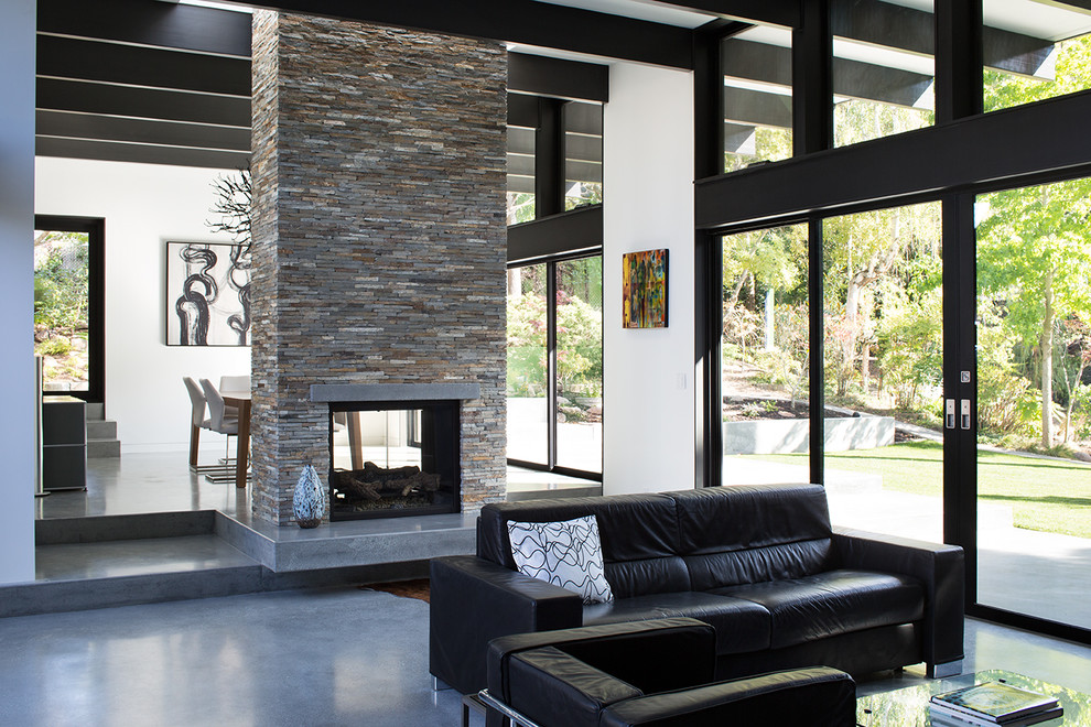 This is an example of a contemporary open concept living room in San Francisco with concrete floors and a two-sided fireplace.