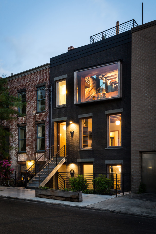 Industrial three-storey brick black townhouse exterior in New York with a flat roof and a shingle roof.