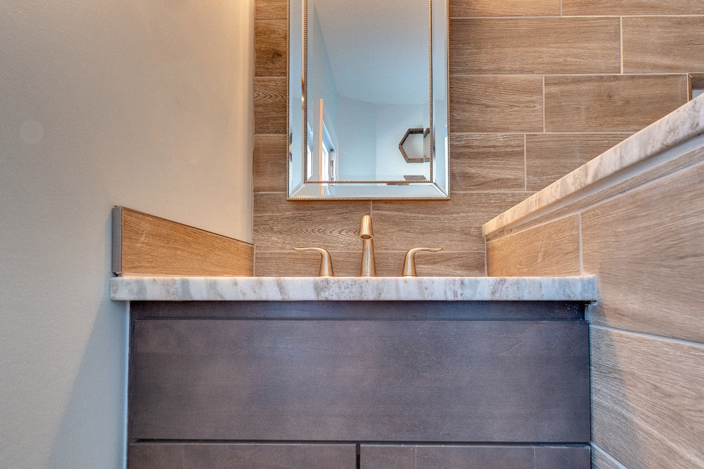 Photo of a mid-sized transitional kids bathroom in Philadelphia with recessed-panel cabinets, medium wood cabinets, a corner tub, a shower/bathtub combo, a two-piece toilet, brown tile, porcelain tile, brown walls, porcelain floors, an undermount sink, limestone benchtops, grey floor, an open shower and grey benchtops.