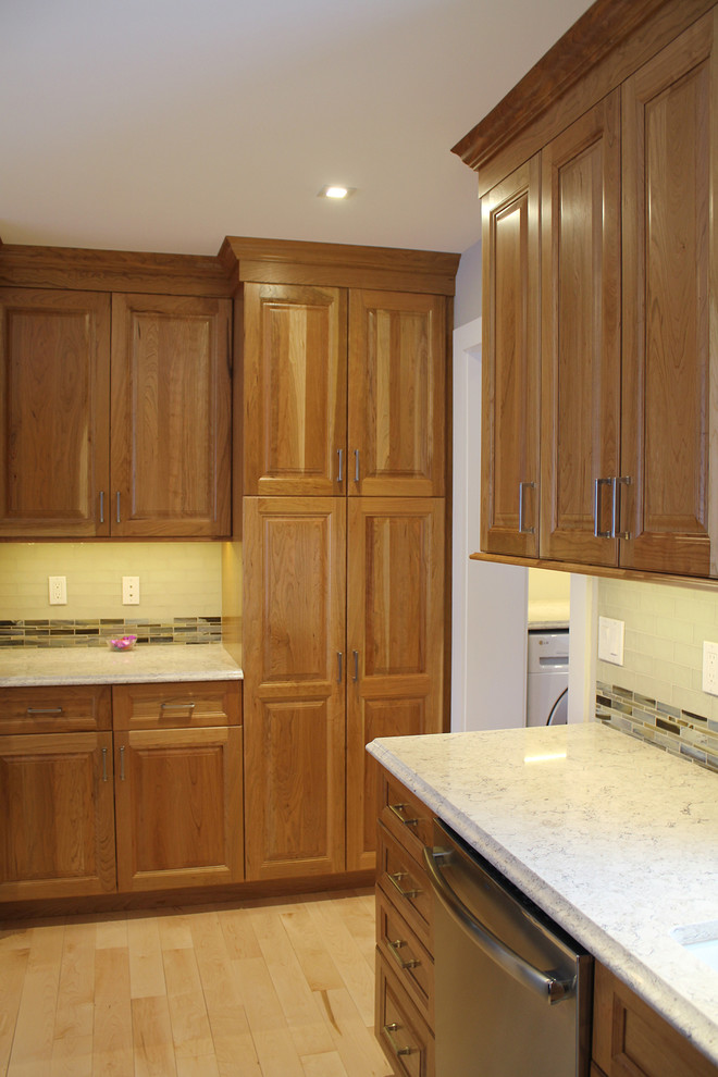Large transitional u-shaped light wood floor and beige floor home design photo in Boston with an undermount sink, raised-panel cabinets, medium tone wood cabinets, quartz countertops, multicolored backsplash, glass tile backsplash, stainless steel appliances, an island and beige countertops