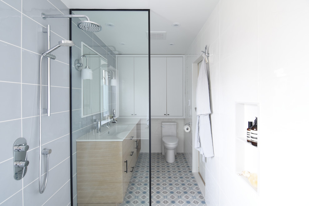 Inspiration for a mid-sized scandinavian master bathroom in Montreal with flat-panel cabinets, light wood cabinets, an alcove shower, gray tile, porcelain tile, grey walls, porcelain floors, a trough sink, multi-coloured floor, a hinged shower door and white benchtops.