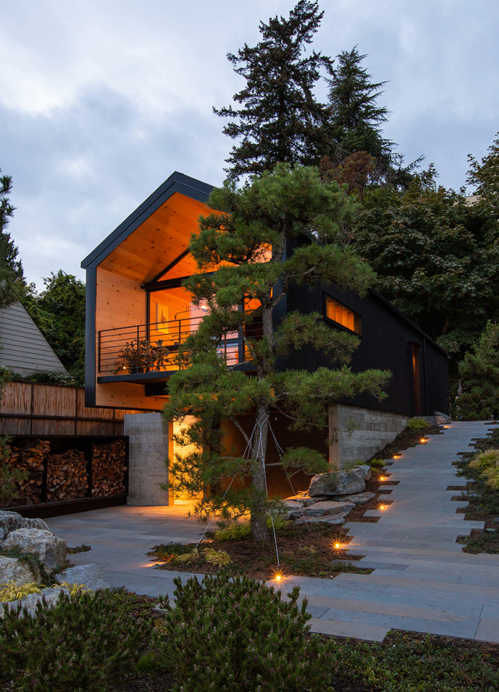 На фото: маленький, двухэтажный, деревянный, черный многоквартирный дом в современном стиле с двускатной крышей, крышей из гибкой черепицы и черной крышей для на участке и в саду с